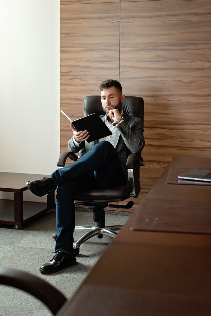 Caucasian man in suit sitting and reading in a stylish office setting.